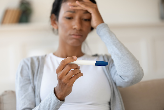 A shocked young woman staring at a pregnancy test because she didn't think she could get pregnant using the pullout method as a form of birth control