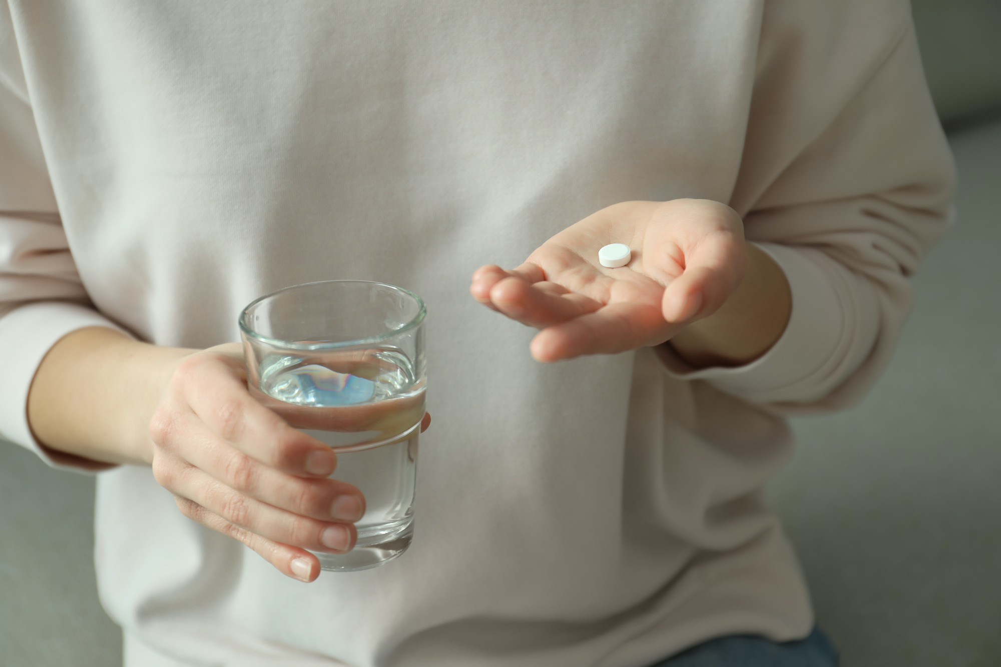 A young woman holding an abortion pill and glass of water