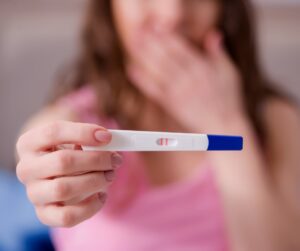 Young woman holding a positive pregnancy test after wondering "How soon after an abortion can you get pregnant?"
